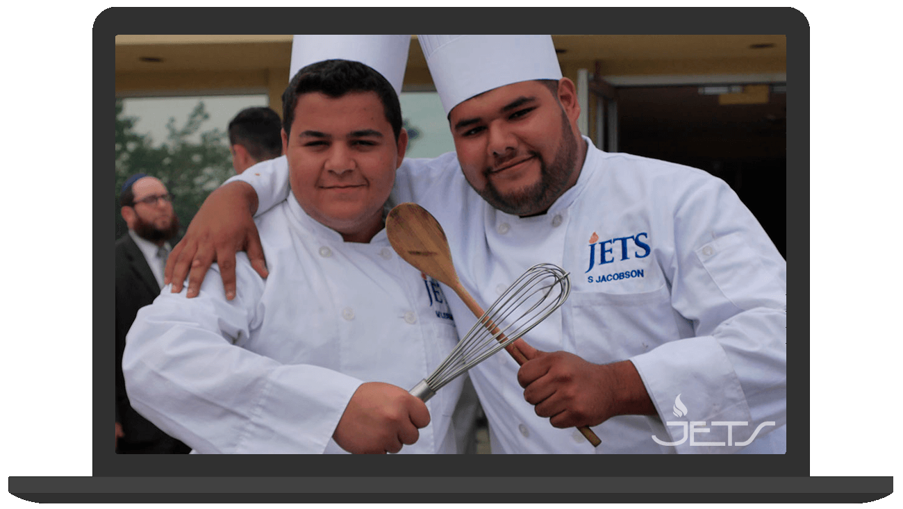 Two people wearing chef's jackets and hats, holding a wooden spoon and whisk