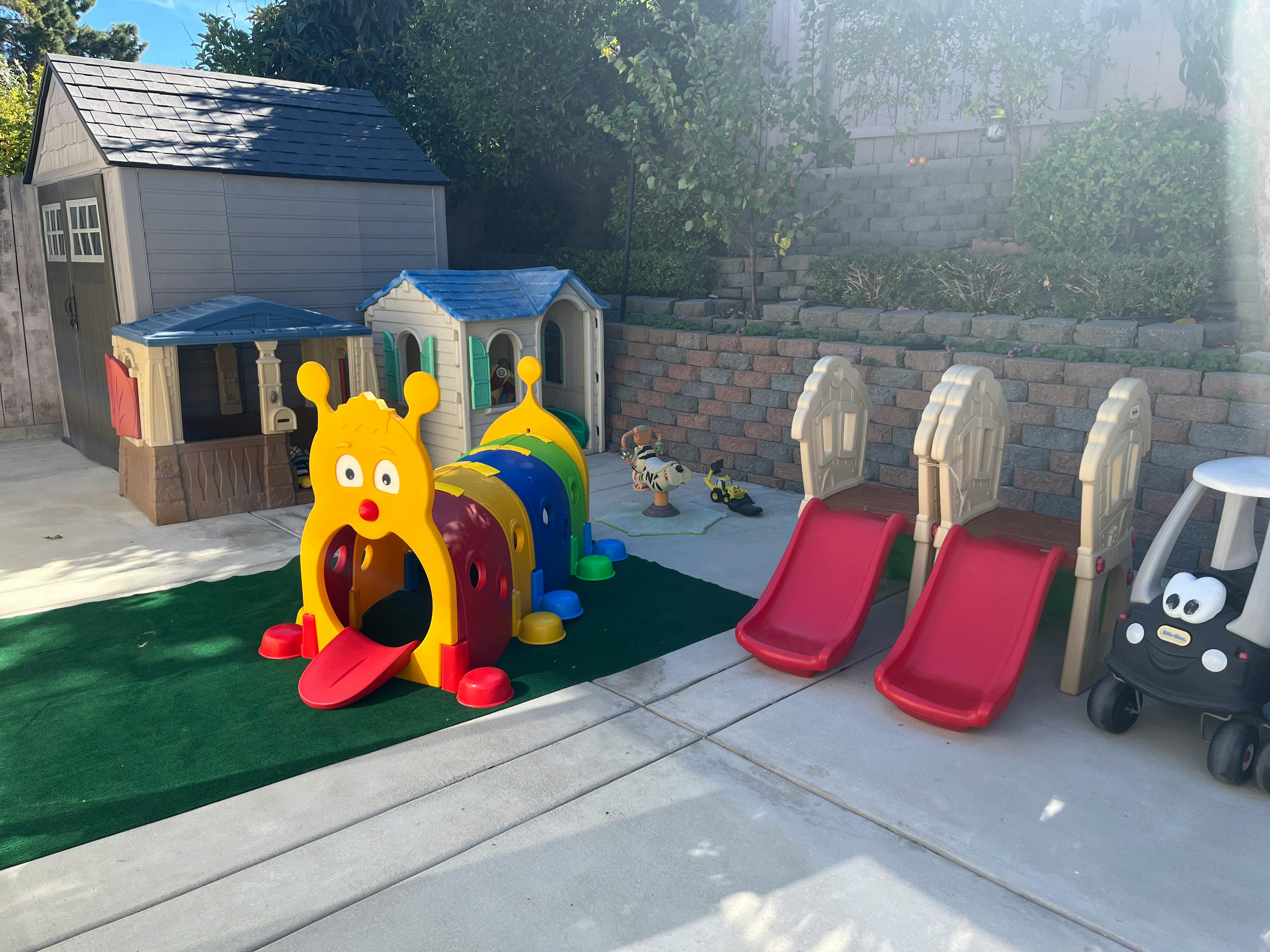 Playground with a caterpillar tunnel, two red slides, and playhouses