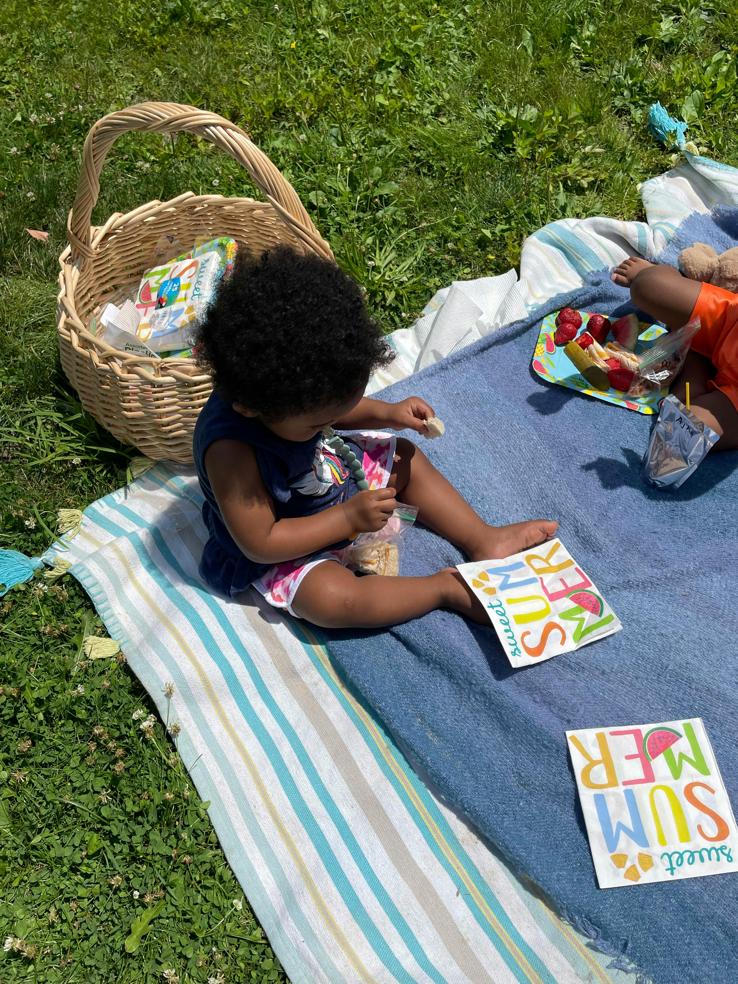 Child sitting on a blanket outdoors, holding a snack bag