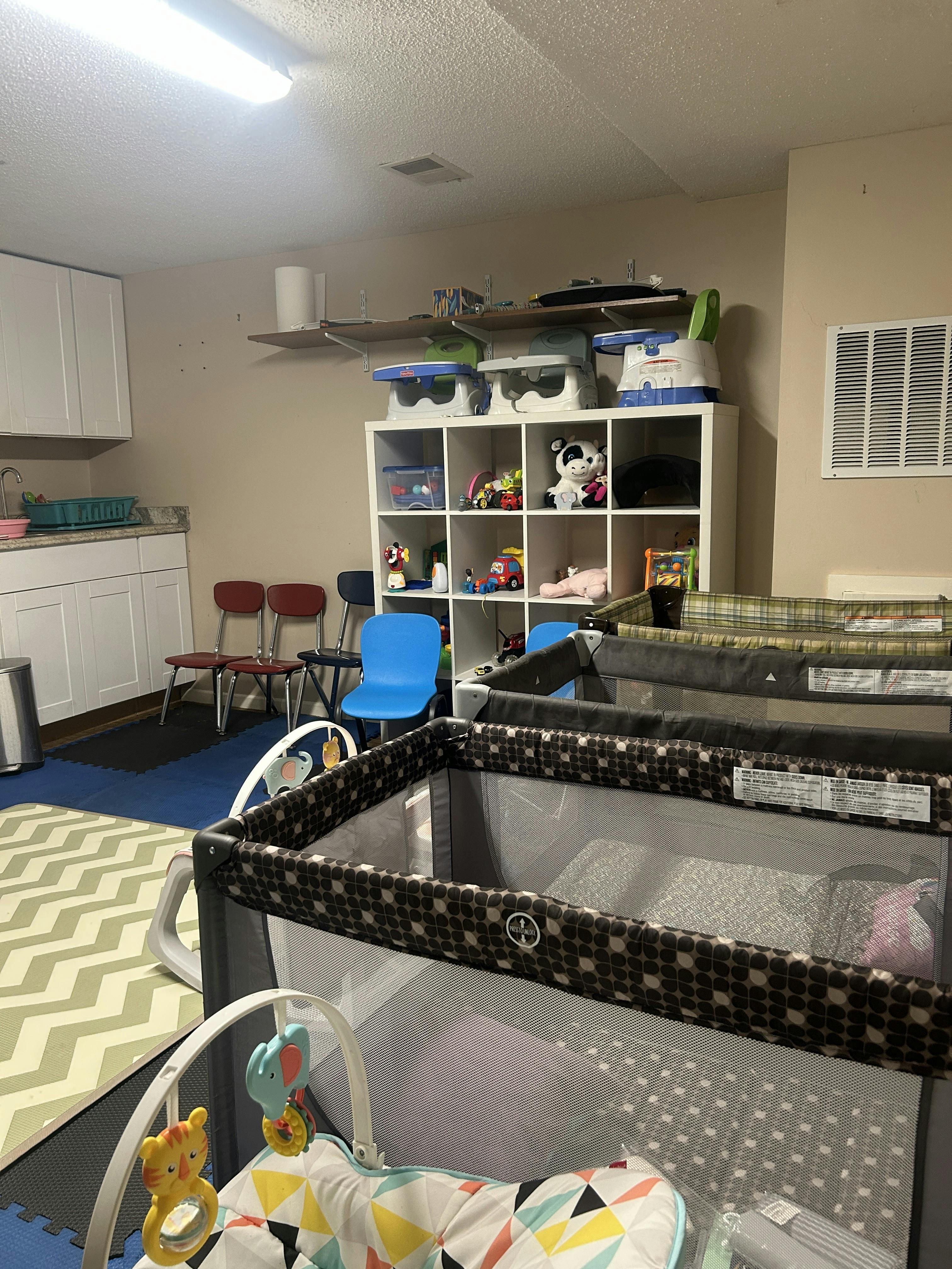 Playroom with multiple cribs, shelves with toys, and small chairs