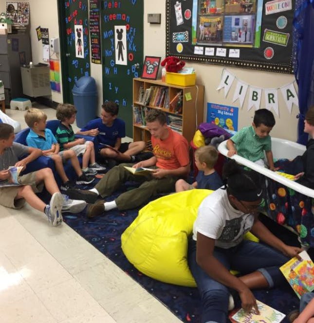 Adult and children reading books on the floor in a classroom