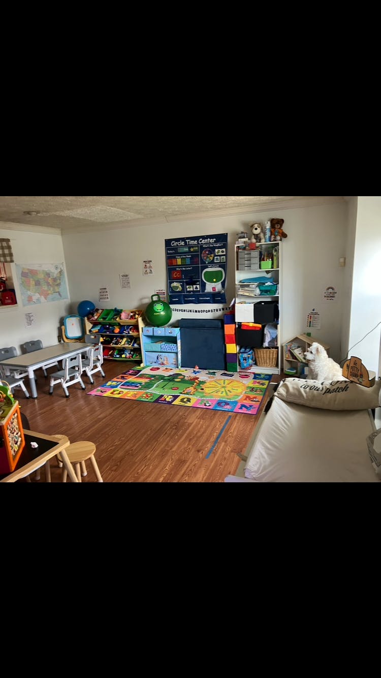 Classroom with a table and chairs, colorful rug, shelves, and a large wall chart