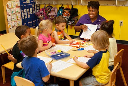 Adult and children sitting at a table with papers and pencils