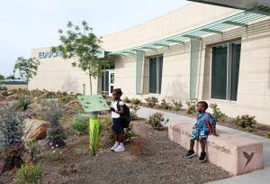 Two children outside a building, one standing and one sitting on a bench