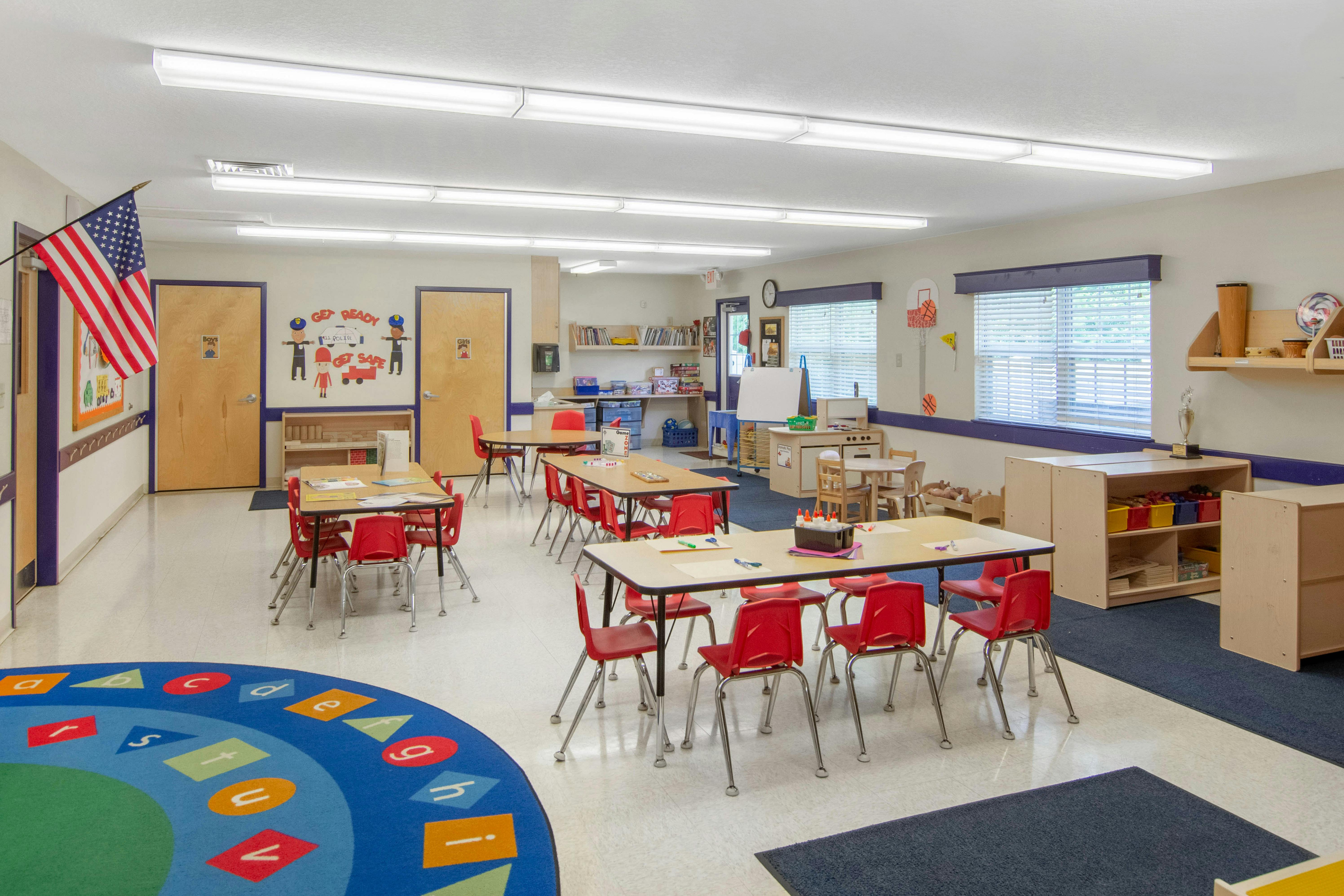 Empty classroom with small tables and red chairs, American flag hanging on the wall