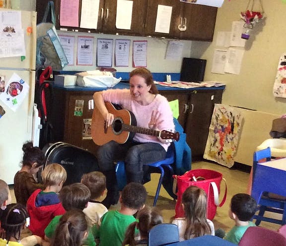 Person playing guitar for a group of children in a classroom
