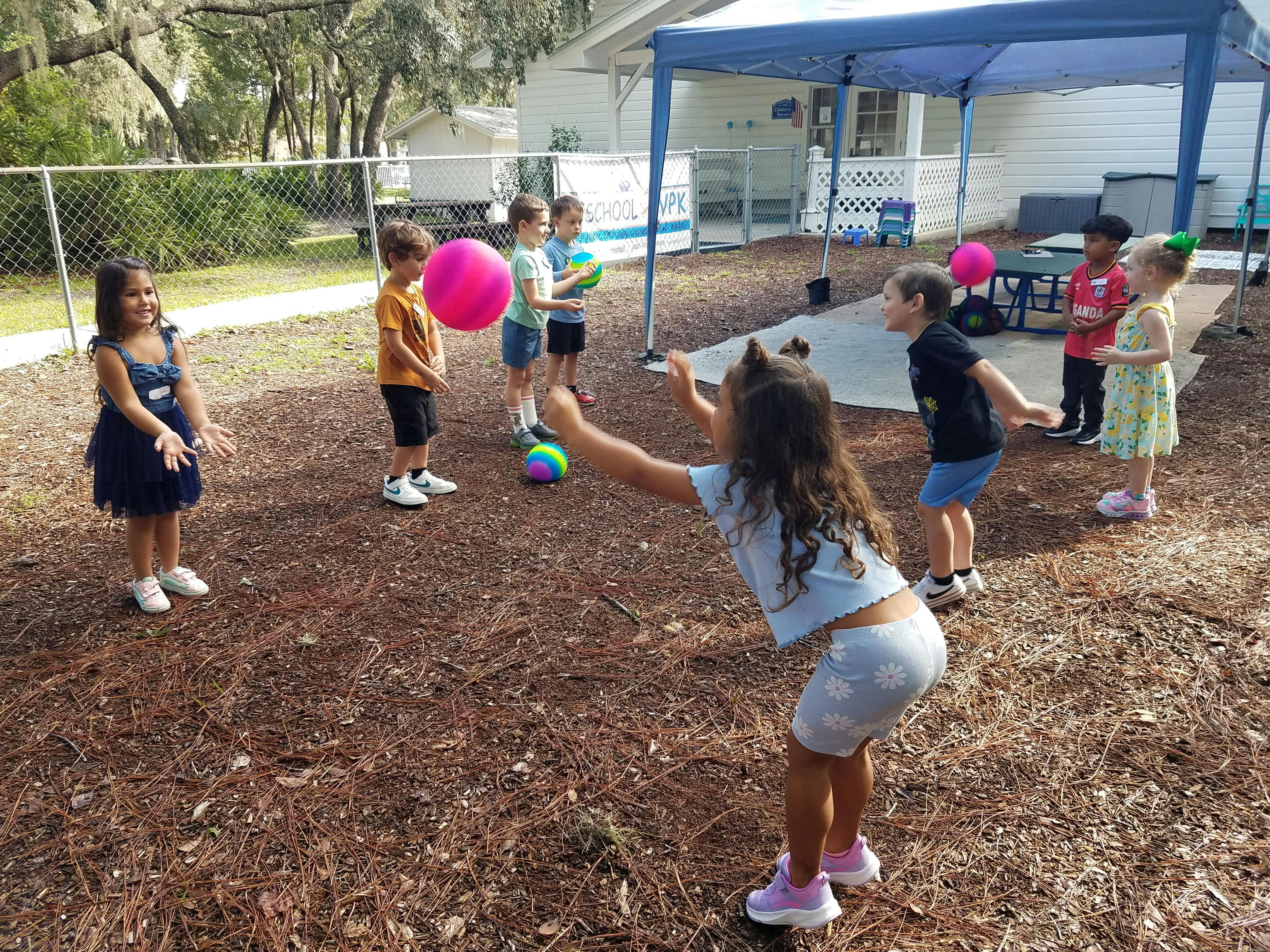 Children playing with balls outside on a ground covered with pine needles
