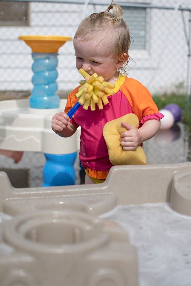 Child holding a yellow sponge and a yellow brush