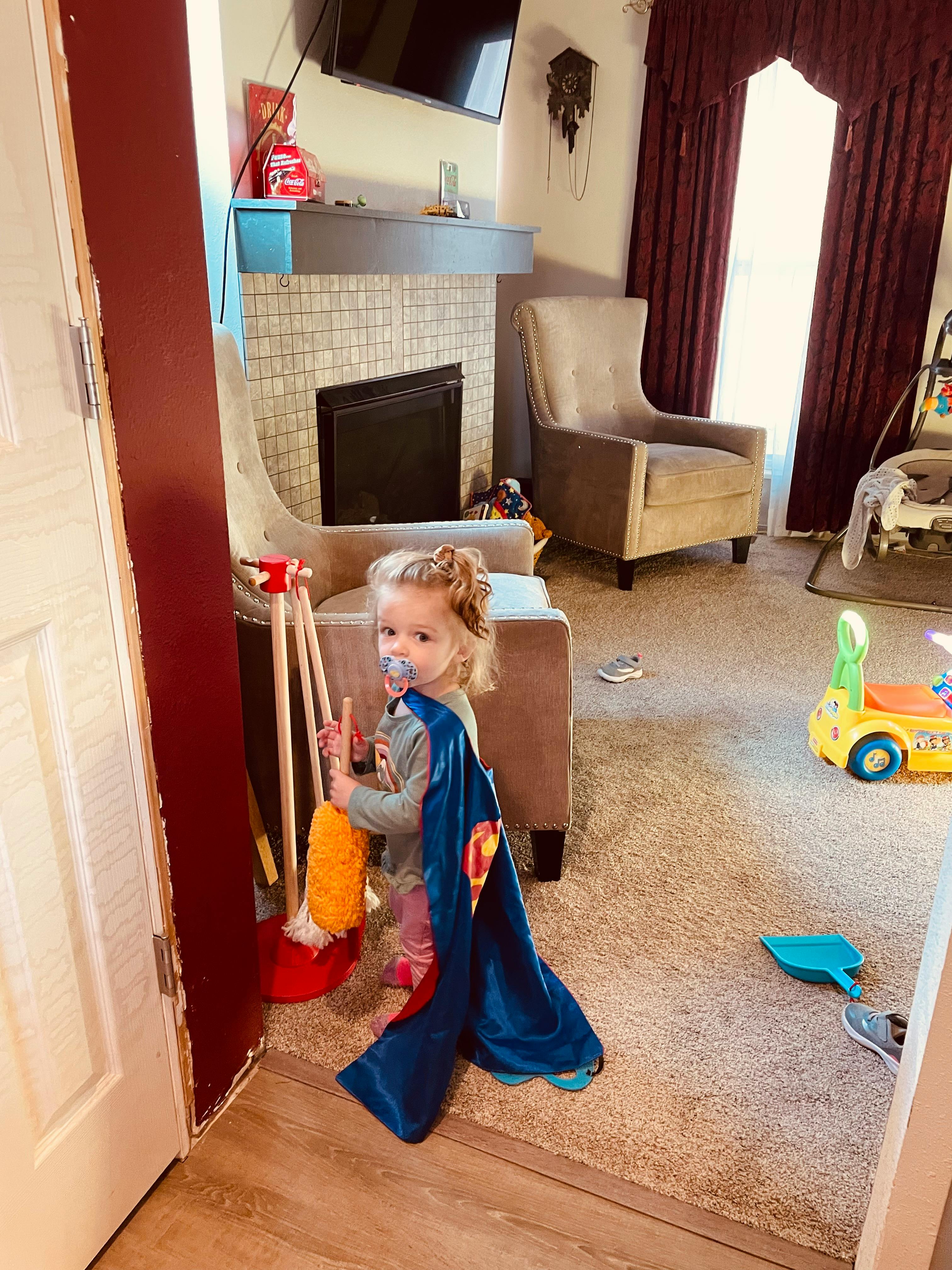 Child in a blue cape holding a toy broom and dustpan