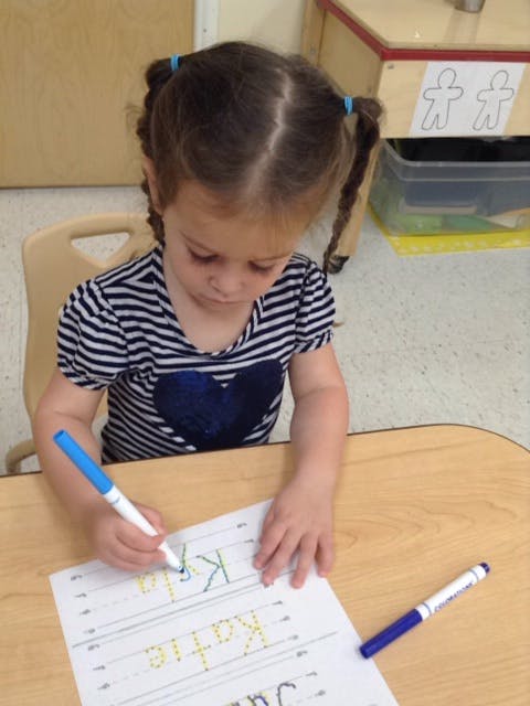 Child writing on paper with a blue marker