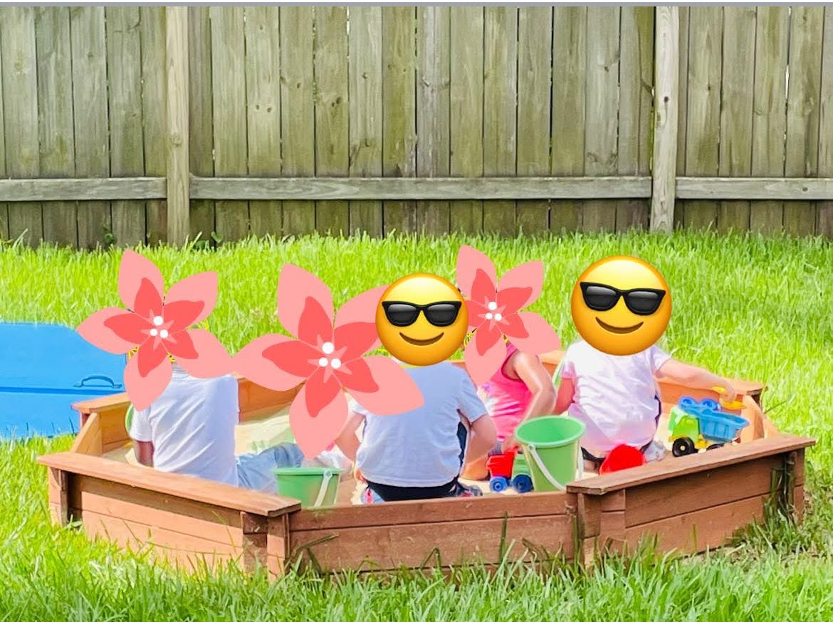 Children playing in a wooden sandbox in a grassy yard