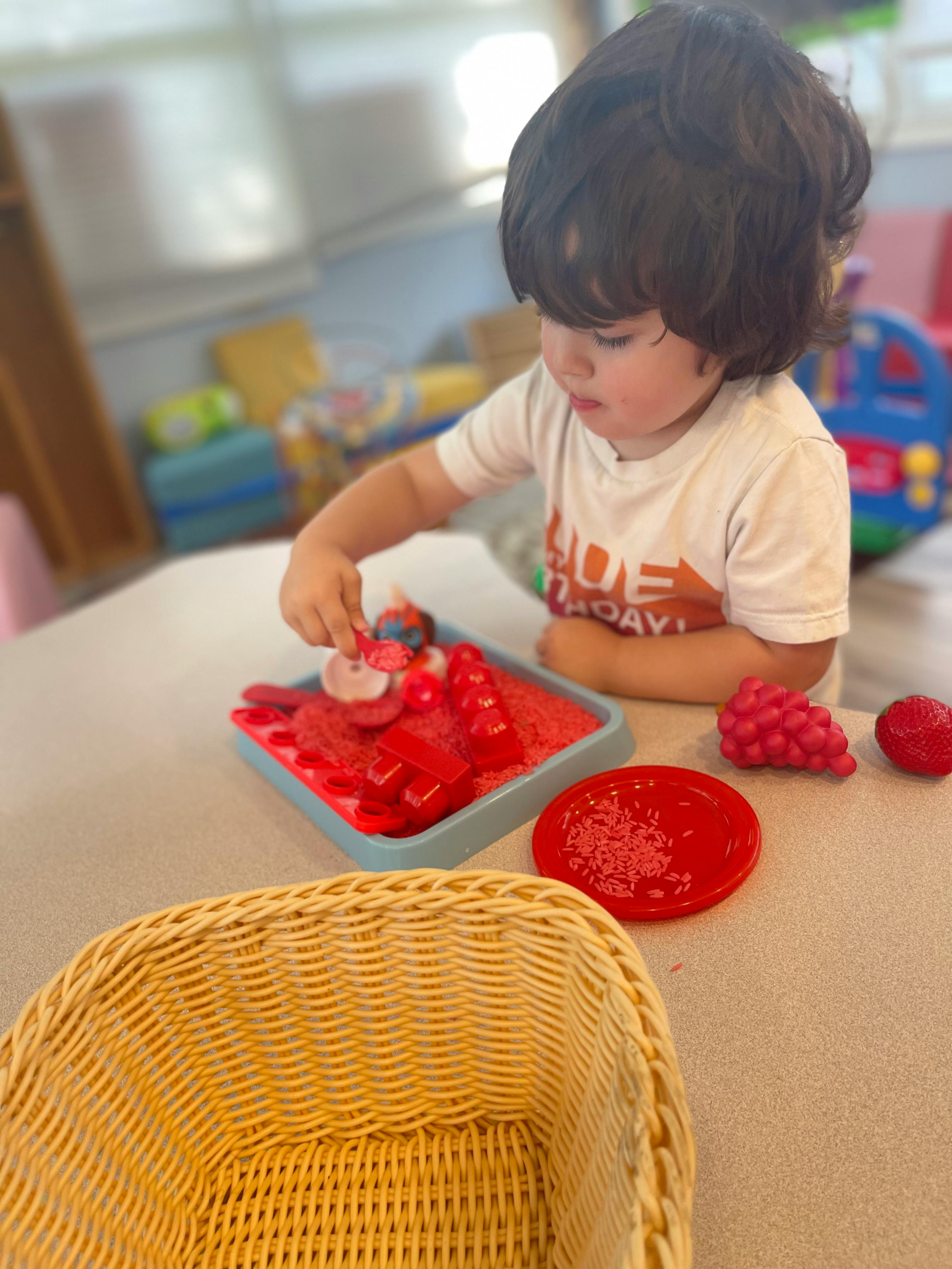Child playing with red sensory bin filler and small toys