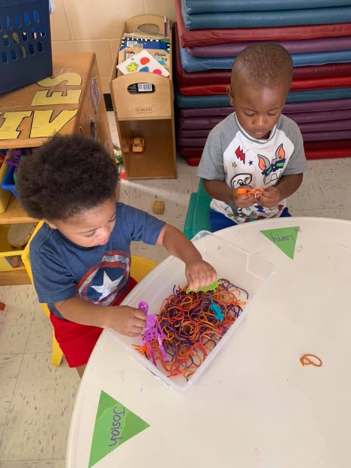 Two children playing with colorful string and toys at a table