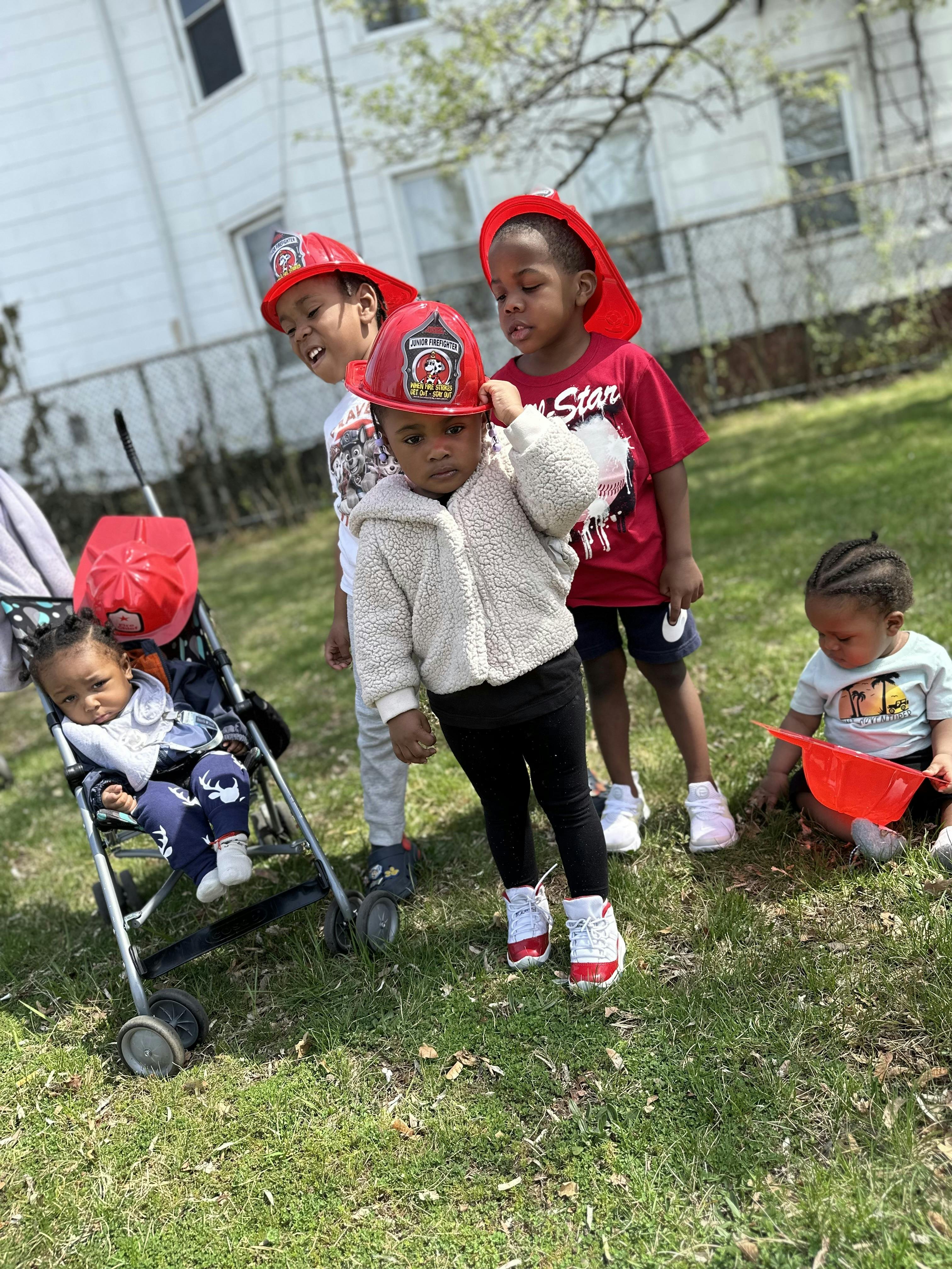 Children playing outdoors, one in a stroller, others standing and sitting