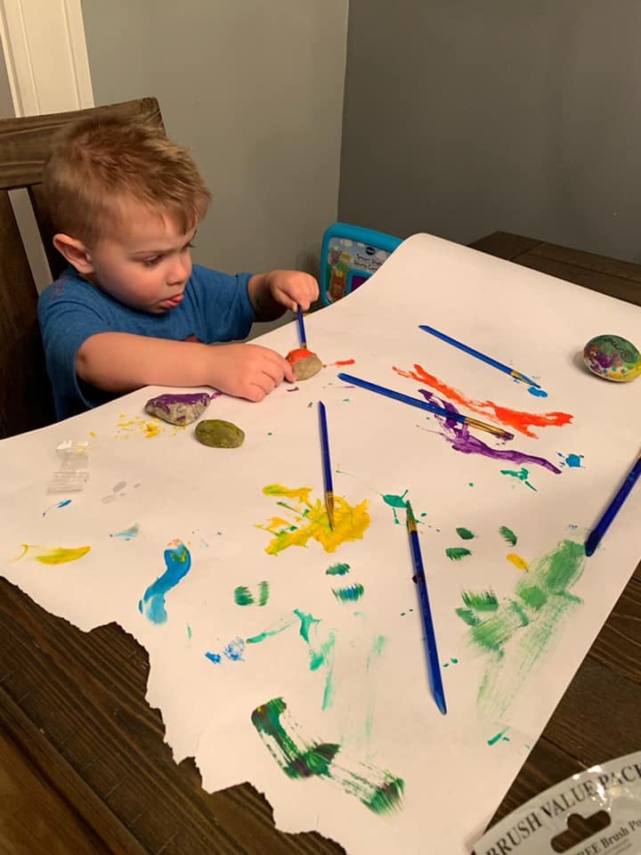 Child painting on a large sheet of paper with brushes and colorful paints