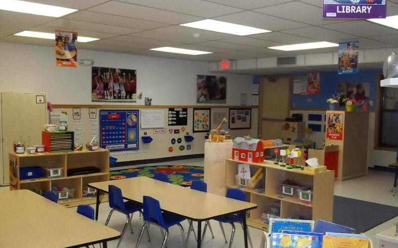 An empty classroom with tables, chairs, shelving units, and a colorful rug