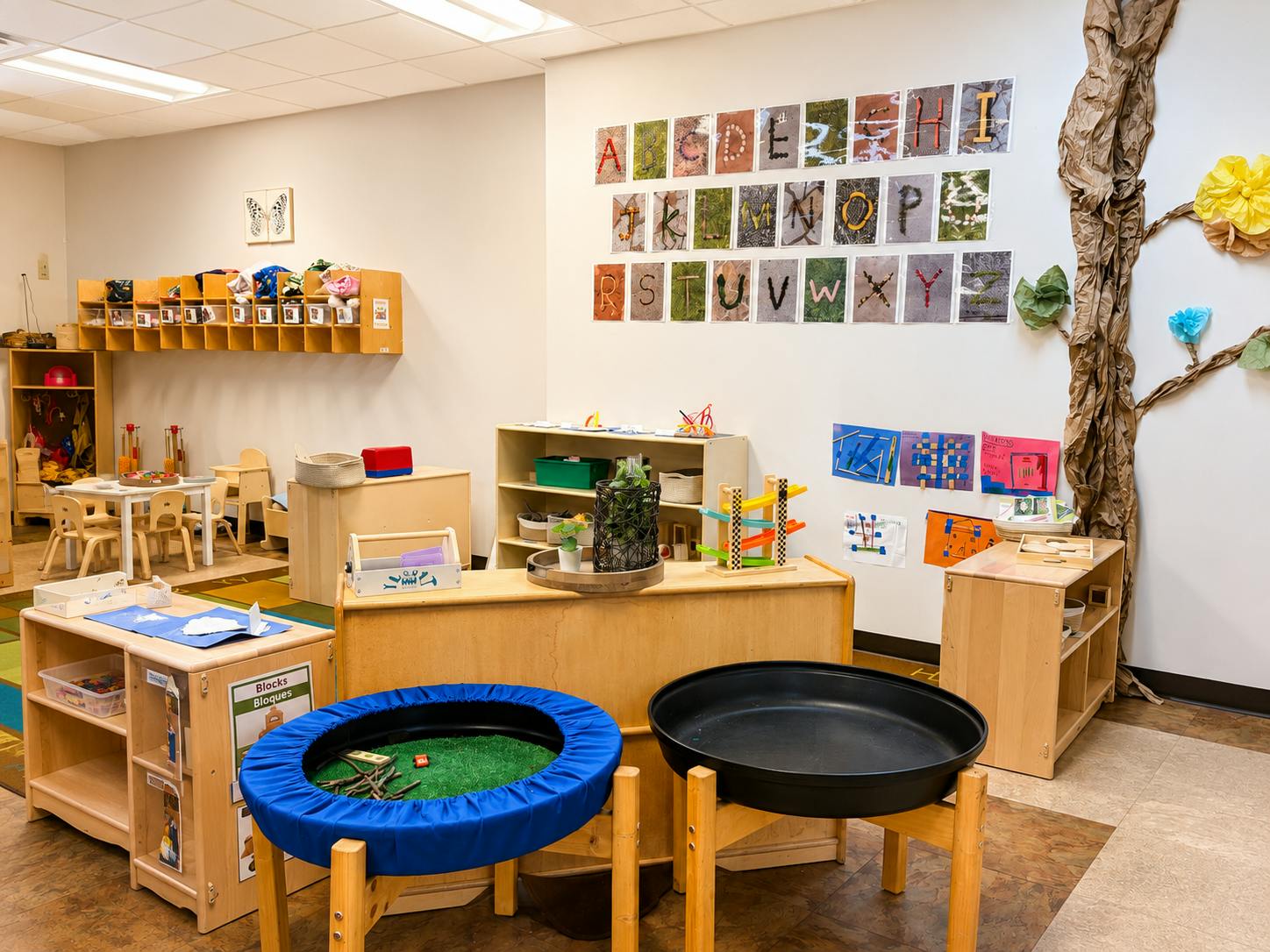 Classroom interior with alphabet wall display, wooden shelves, and play tables