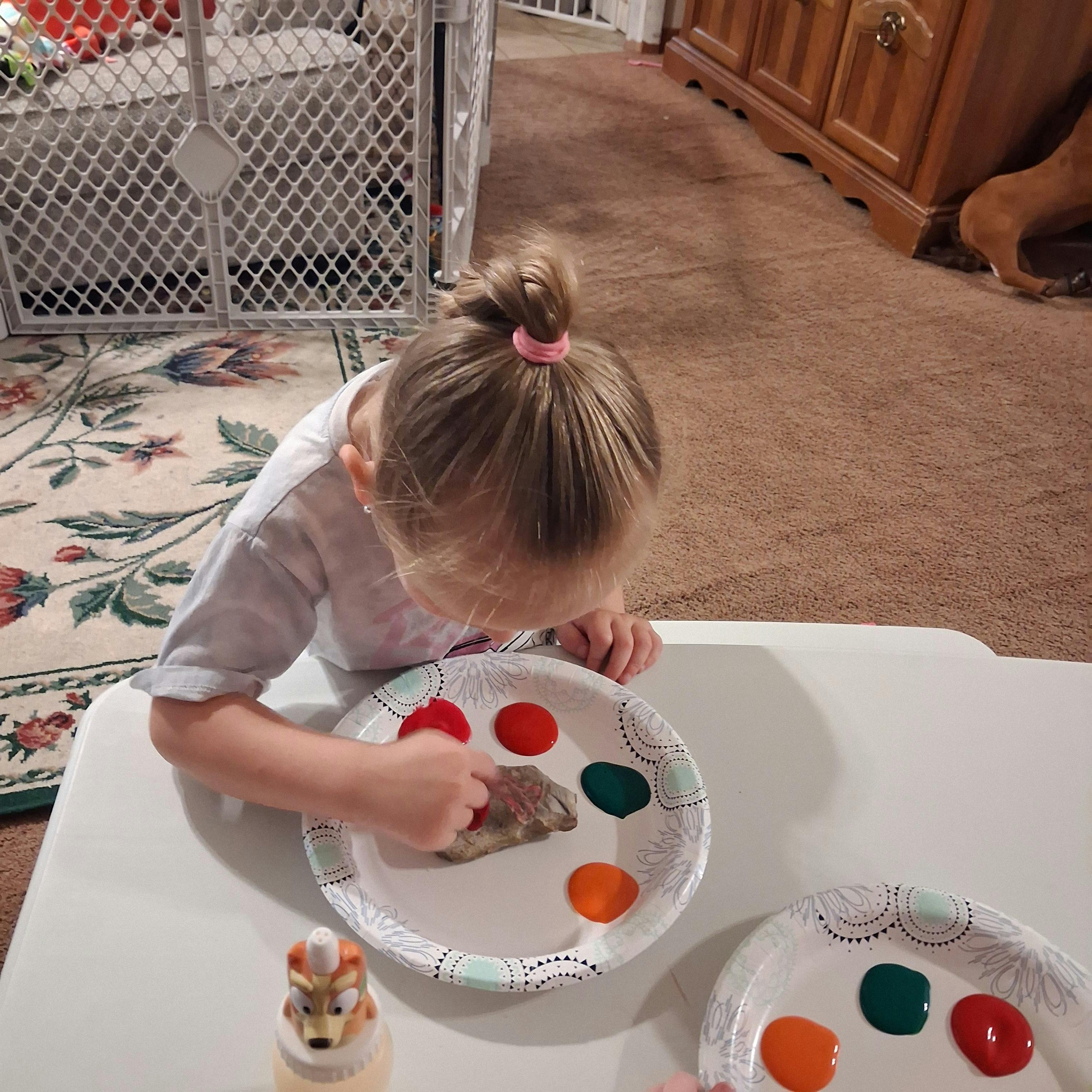 Child painting a rock with colors on a paper plate