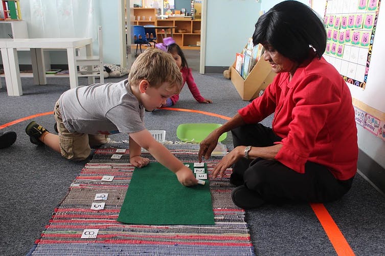 Adult and child on floor playing with cards in a classroom