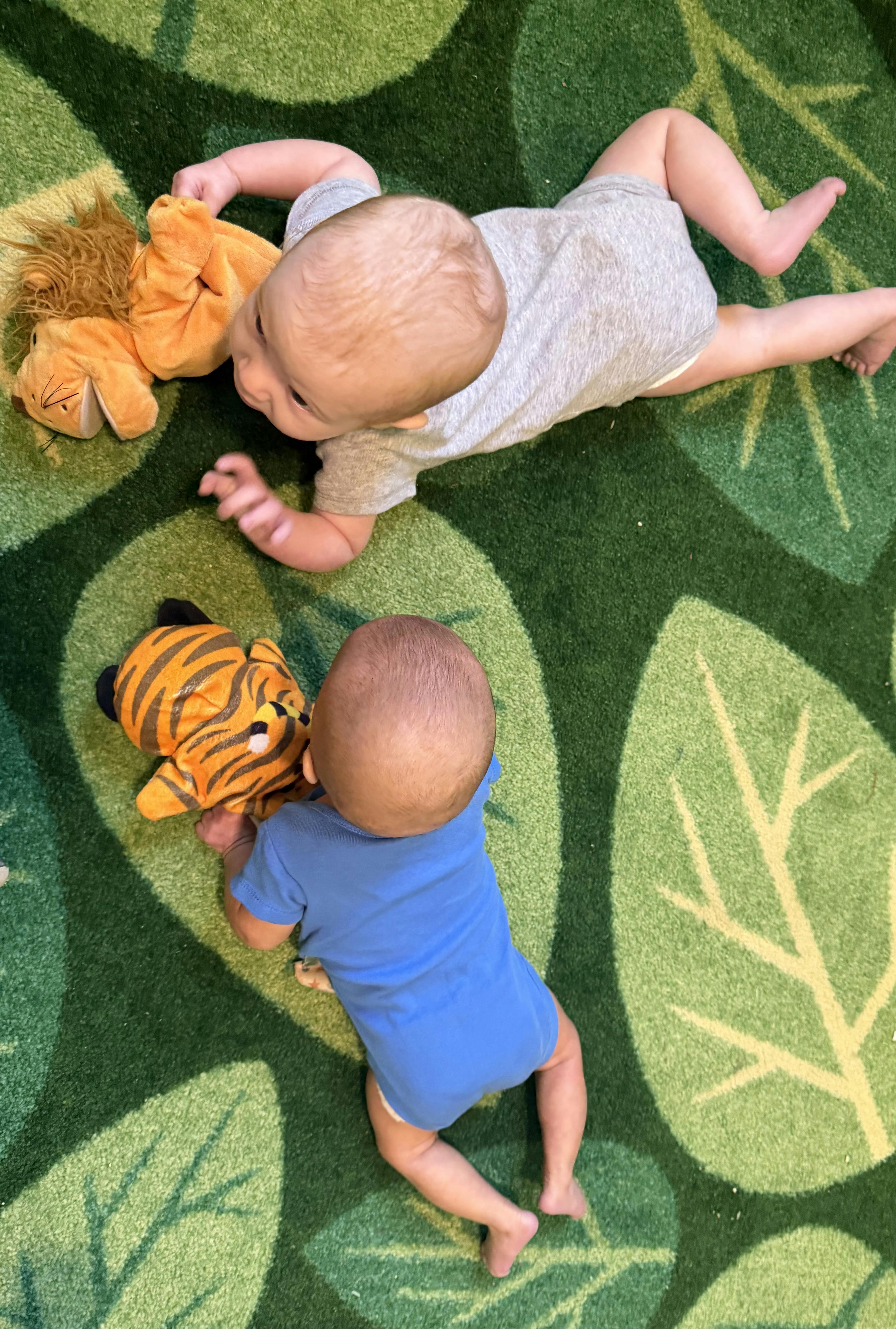 Two children crawling on a leaf-patterned rug with plush toys