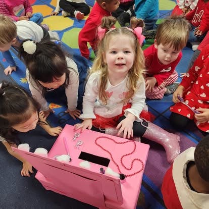 Child sitting on floor with a pink box, surrounded by other children