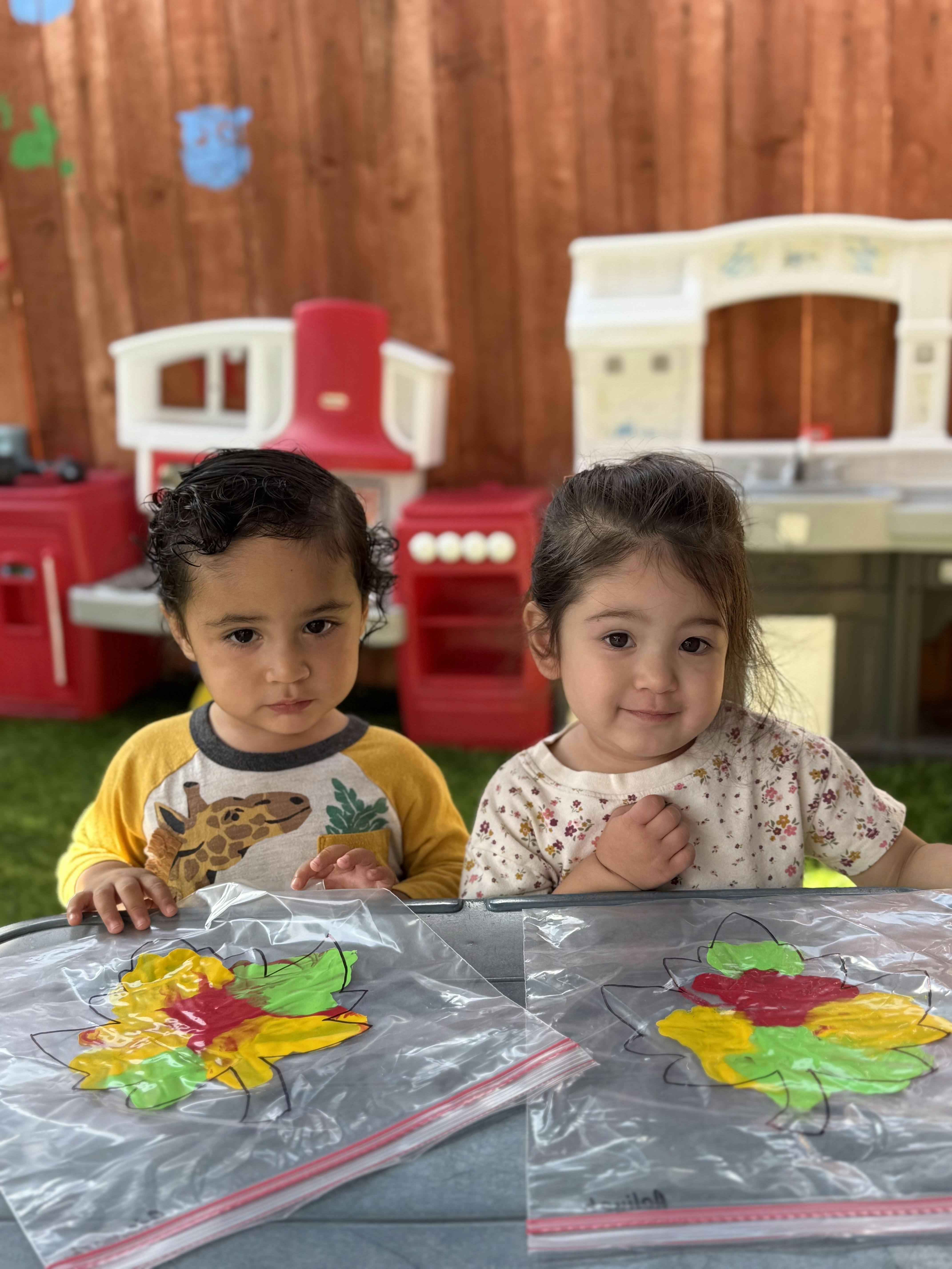 Two children painting in plastic bags at a table