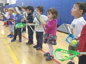 Children holding lacrosse sticks with balls in a gym