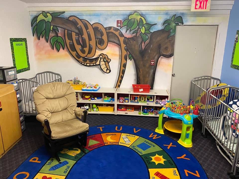 Nursery room with cribs, a rocking chair, and a colorful alphabet rug