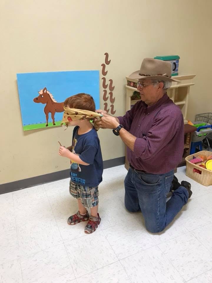 Person blindfolding a child in front of a horse drawing