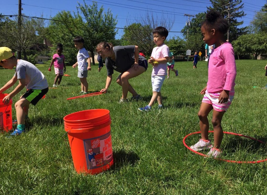 People and children playing with buckets and hoops on a grassy field