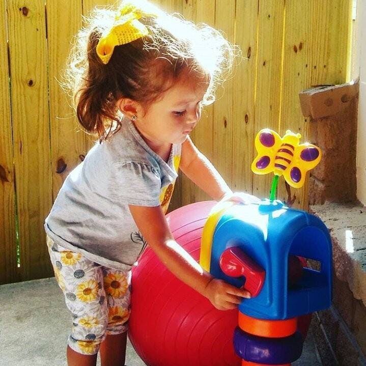 Child playing with a toy mailbox and a large red ball