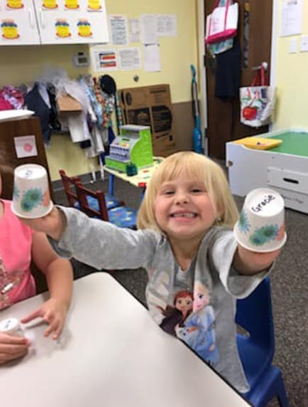 Child holding up two decorated paper cups