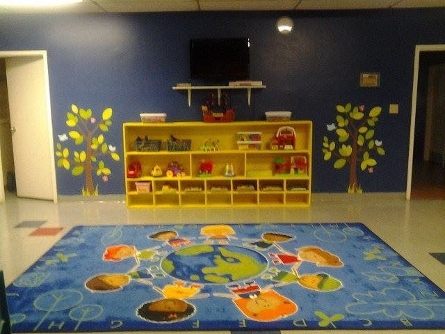 Classroom with blue walls, yellow shelving unit, and blue rug with world map