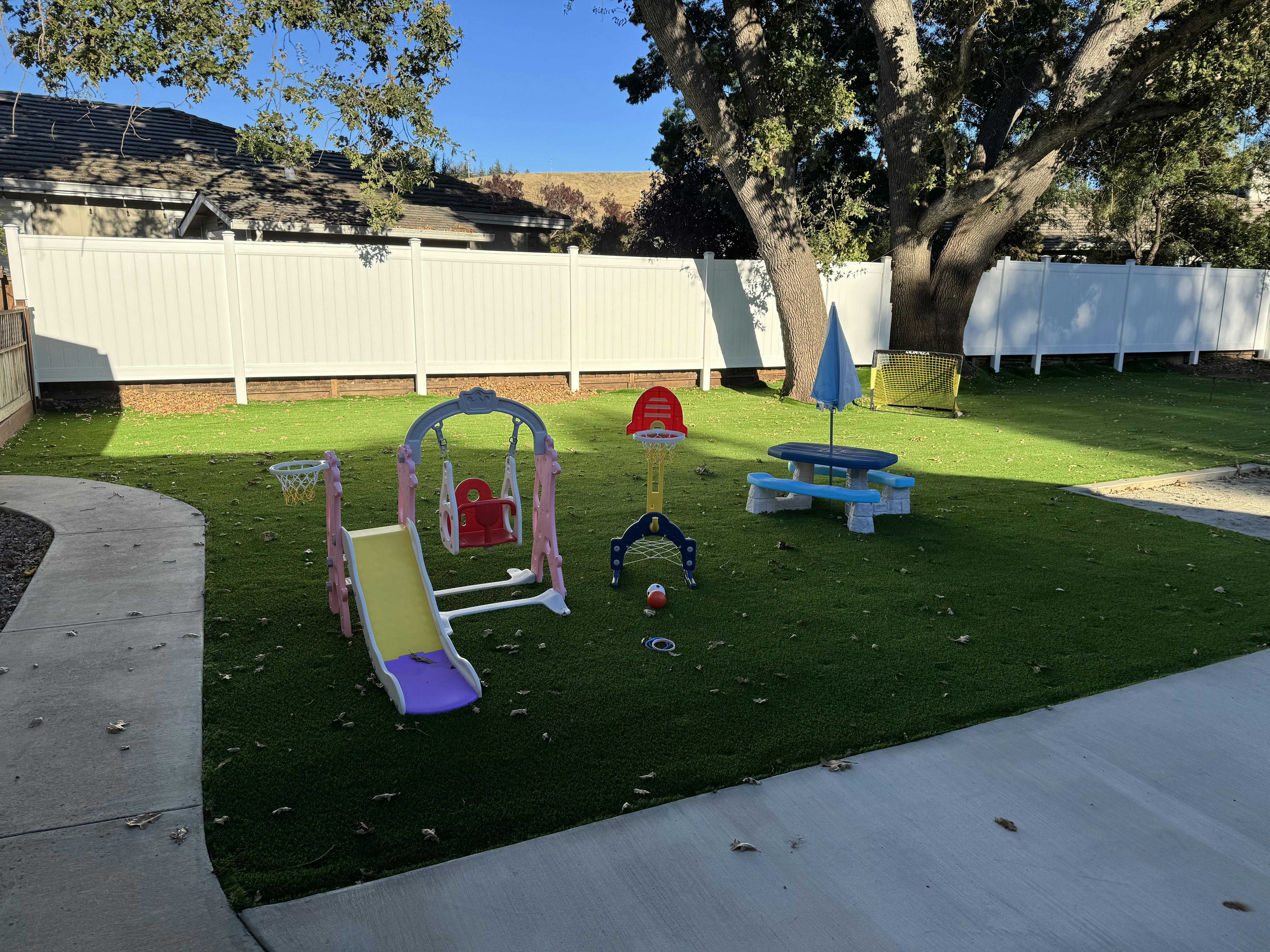 Playground with slide, swing, basketball hoop, and picnic table on grass
