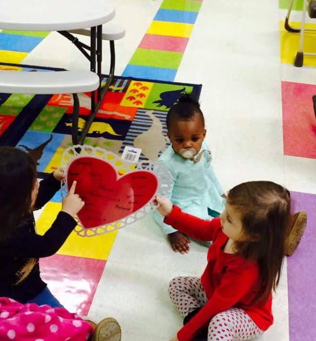 Three children on the floor holding a red heart decoration