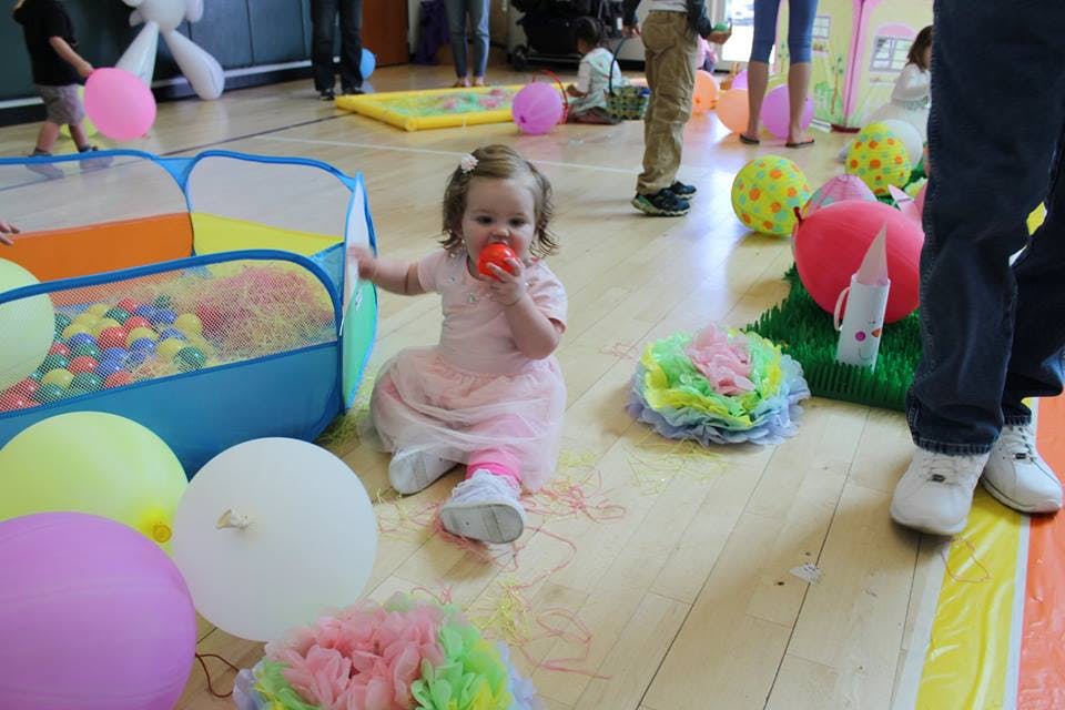 Child sitting on floor with toy near ball pit and balloons