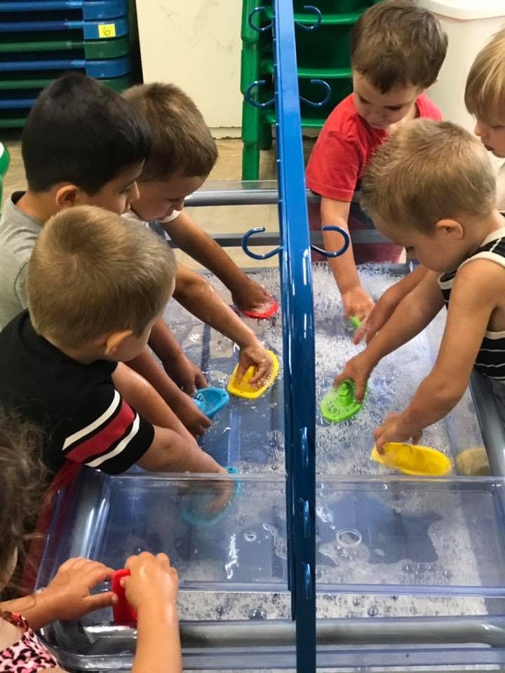 Children playing with toy boats in a water table