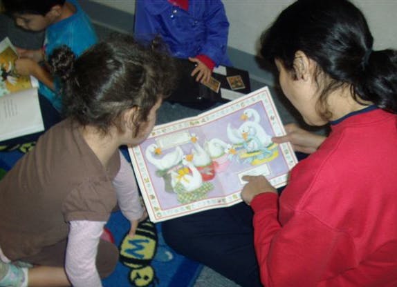 Person and child looking at an open book with illustrations