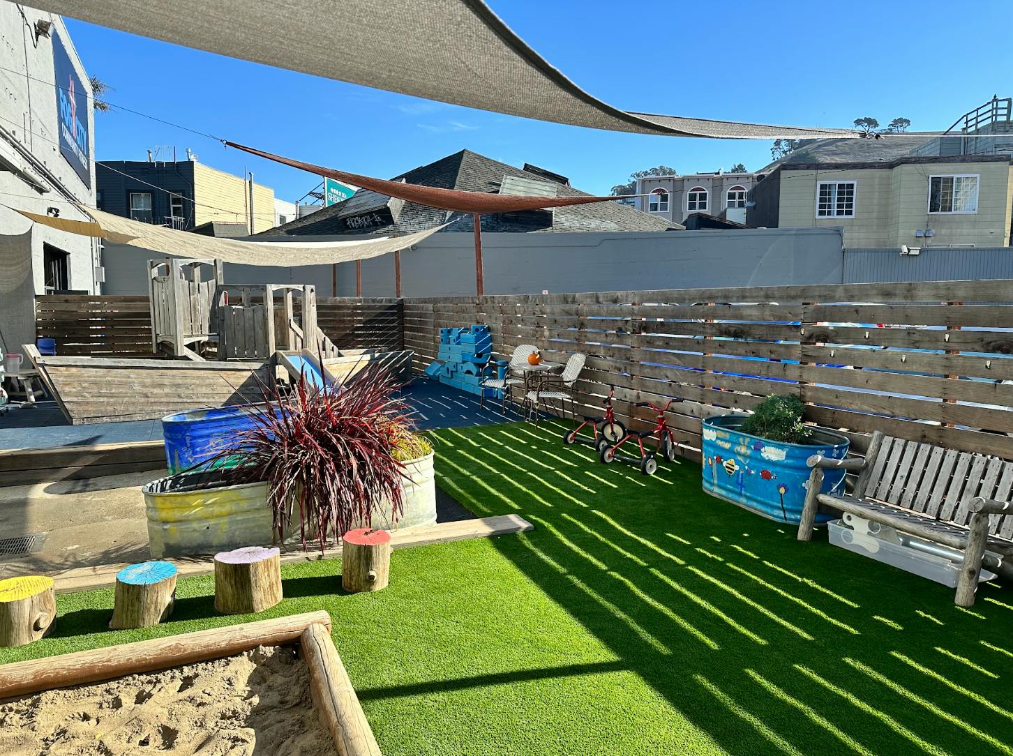 Outdoor play area with artificial turf, shade sails, and wooden fence