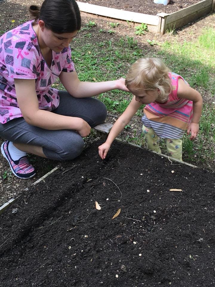 Person and child planting seeds in a garden bed