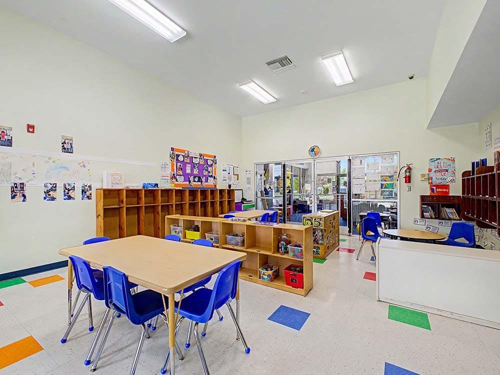 Empty classroom with small tables and chairs, shelves, and colorful floor tiles