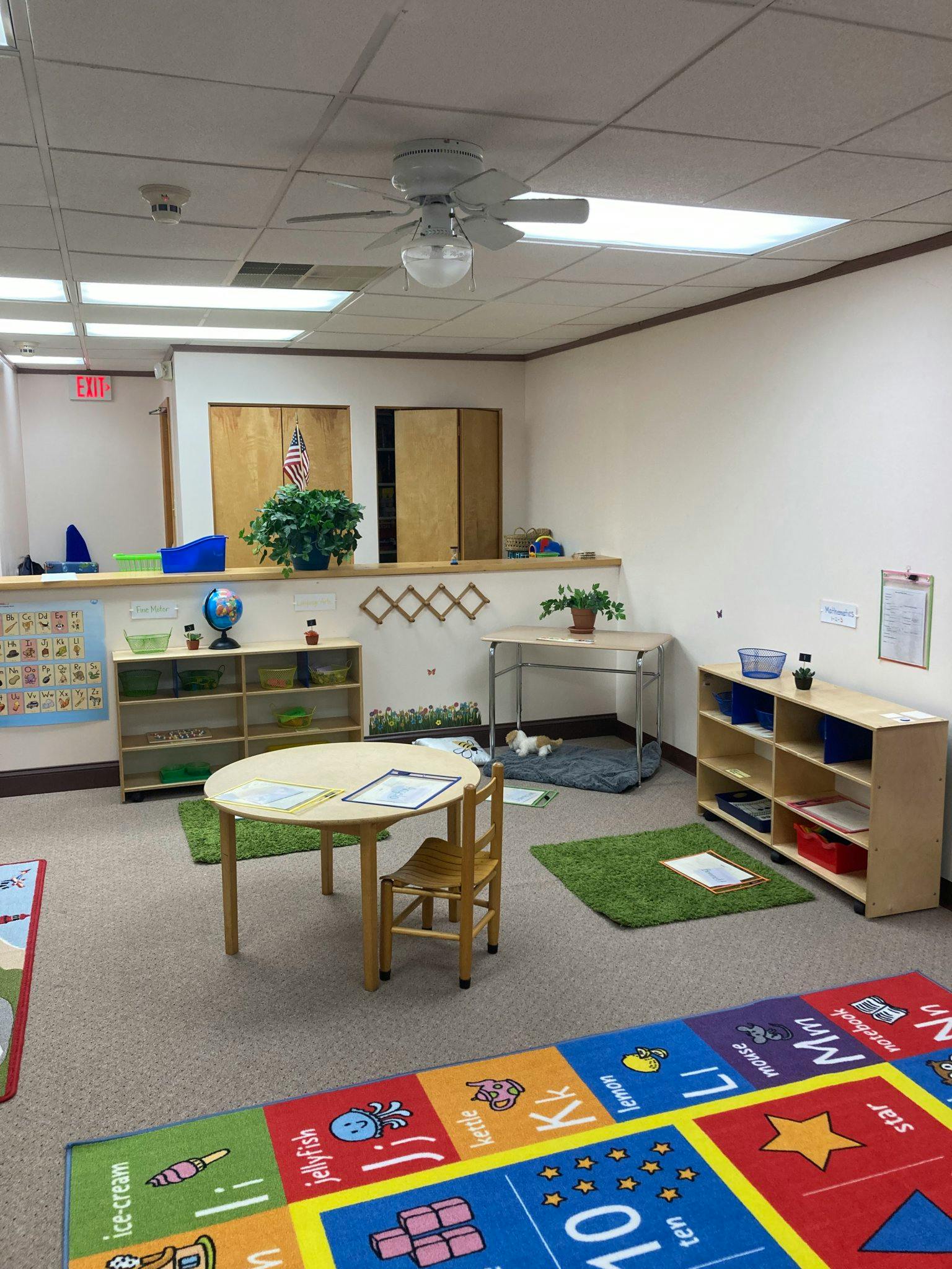 Classroom with small tables, chairs, shelves, and colorful rugs