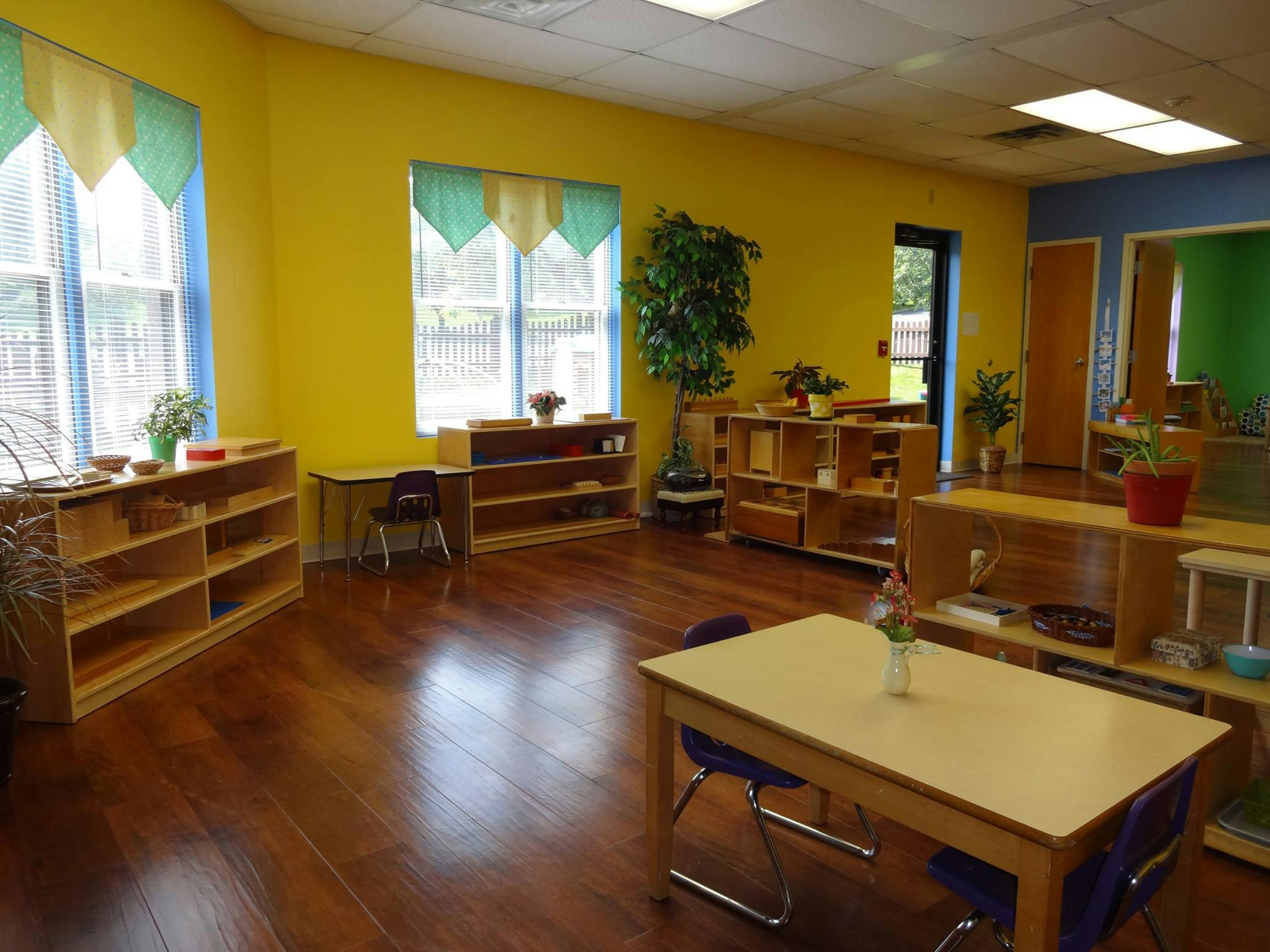 Empty classroom with yellow walls, wooden shelves, and small tables