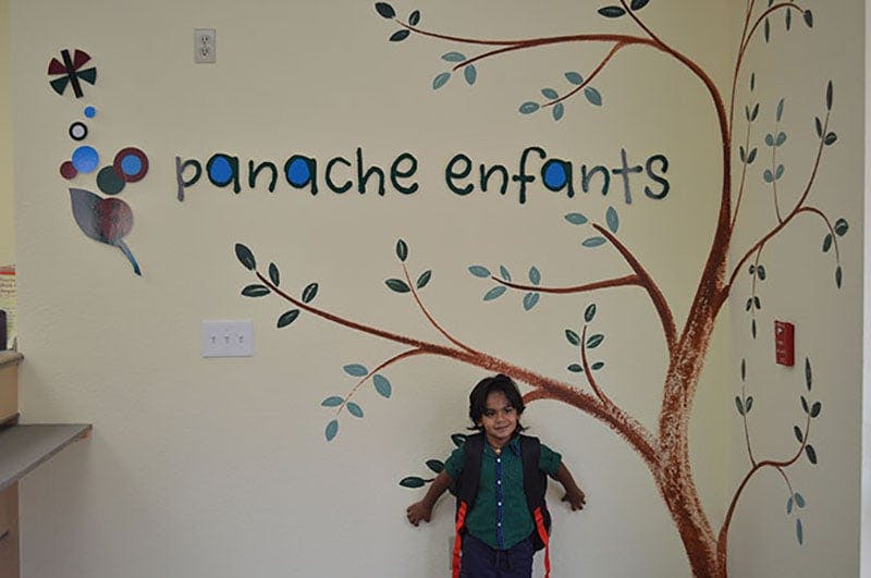 Child standing in front of a wall with a painted tree and "panache enfants" text