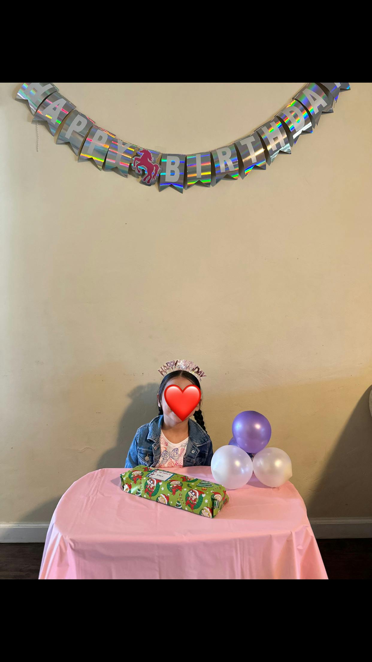 Child wearing a crown, sitting at a table with balloons and a gift