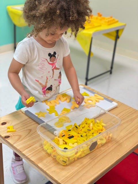 Child playing with yellow letter and shape cutouts on a table