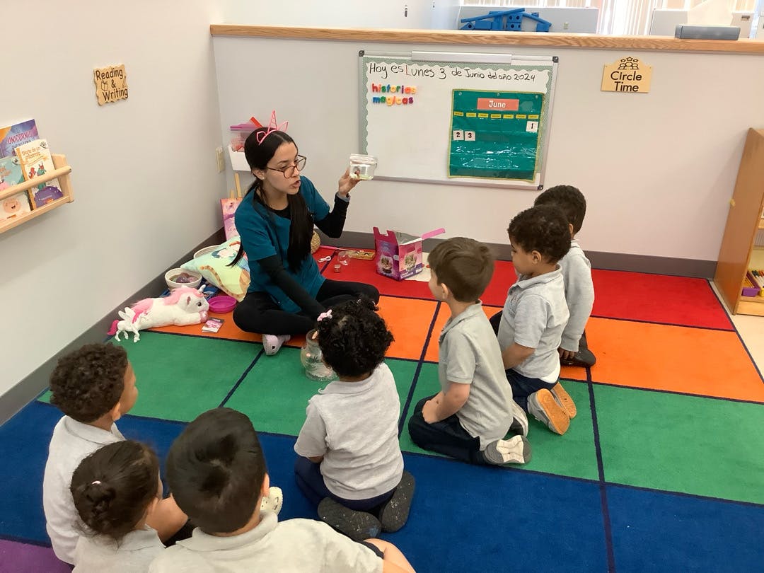 Adult teaching a group of children sitting on a colorful rug in a classroom