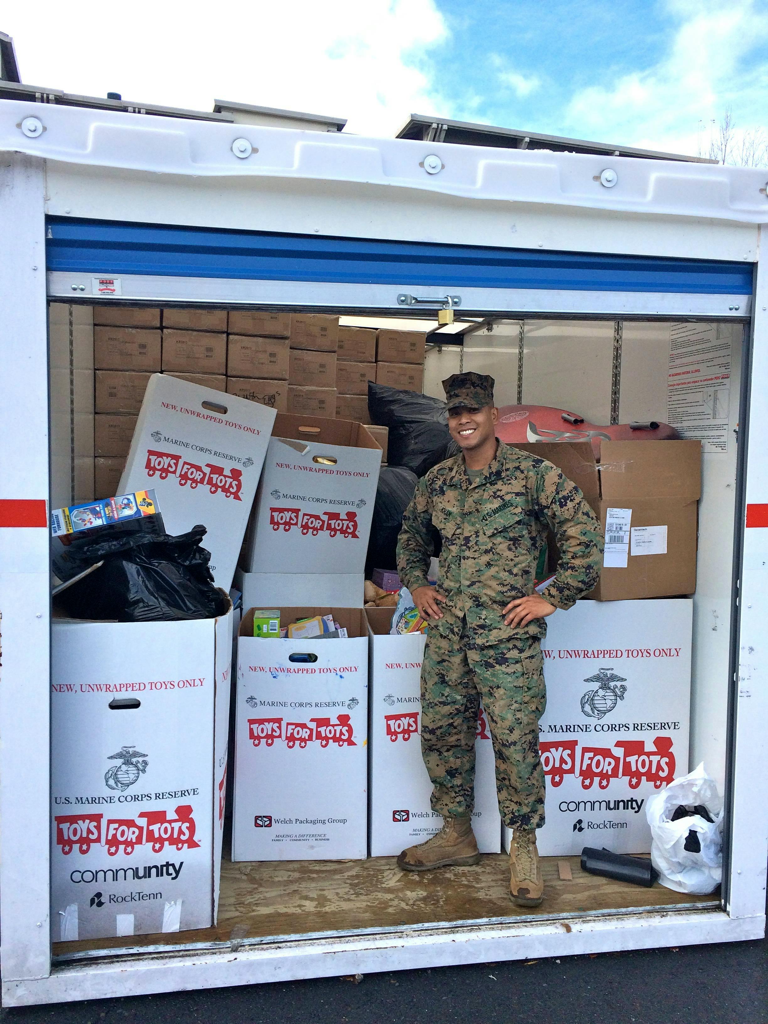 Person in camouflage uniform standing in a storage unit filled with Toys for Tots boxes
