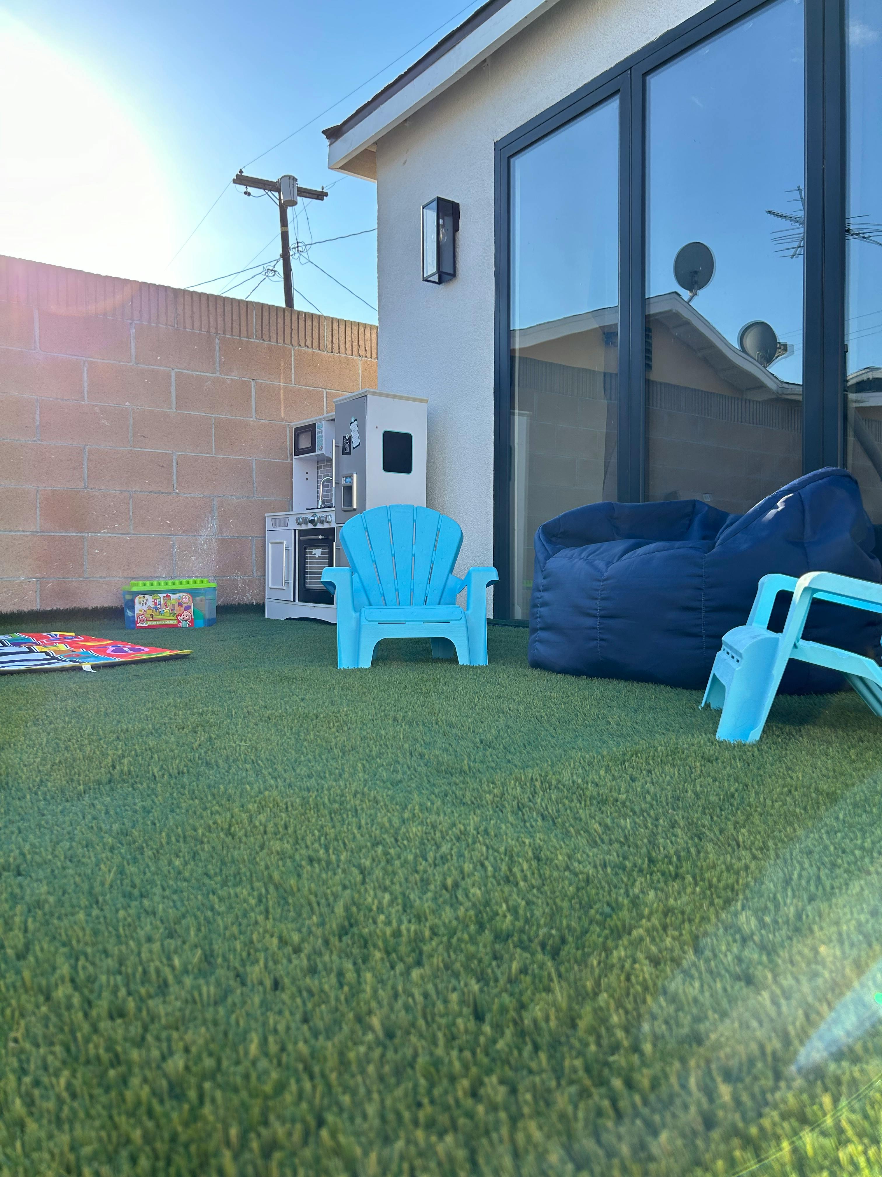 Outdoor patio with artificial grass, blue chairs, and a play kitchen