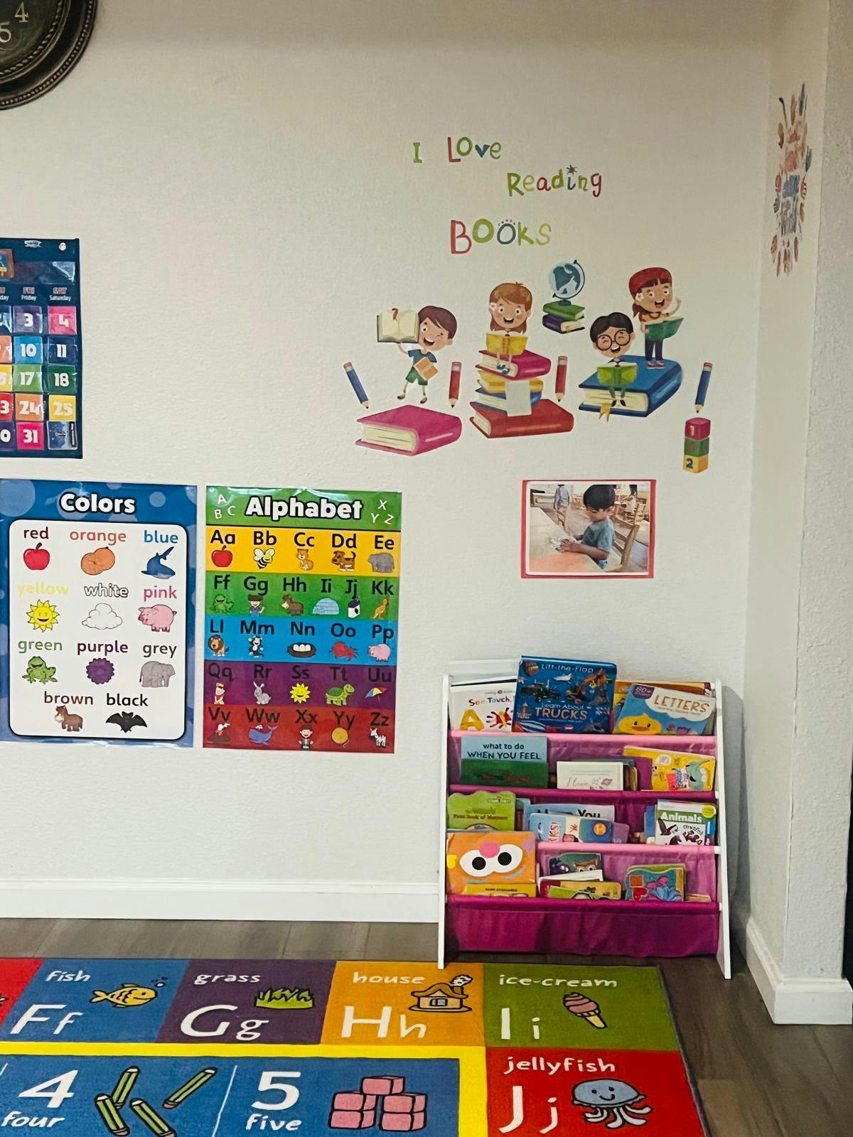 Classroom wall with educational posters, book rack, and alphabet rug